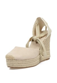 Sandalia de cuña beige de espadrilla con un upper de tejido texturizado, puntera cerrada y atadura en el tobillo. Presenta una plataforma y un tacón en cuña envueltos en yute.
