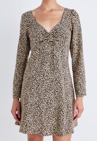 Robe à manches longues beige ornée d'un imprimé léopard noir, avec un profond décolleté en V et un détail noué au niveau de la poitrine. Tissu doux, coupe évasée.