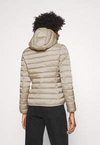 Vaaleanruskea puhvijakku hupulla, jossa on vaakasuoraa ompelua eristyksen takaamiseksi ja elastiset hihansuut tiiviin istuvuuden saavuttamiseksi.