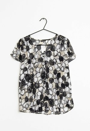 Kortærmet bluse i gennemsigtigt stof med et mønster af sorte og hvide cirkler, med V-udskæring og knapdetalje foran.