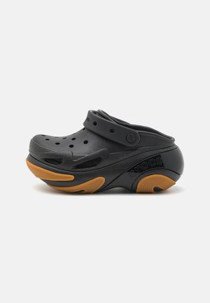 Sort Crocs clog med orange tekstureret sål, ventilationshuller og justerbar hælrem, vist fra siden på hvid baggrund.
