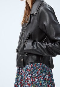 Svart lädermotorcykeljacka med en kort design, med en notch-krage, fickor med blixtlås och en mjuk yta.