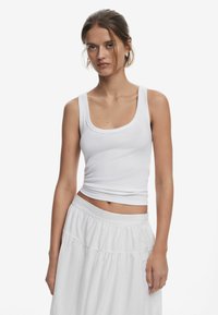 White ribbed tank top with a scoop neckline, fitted design, paired with a flowy, tiered white skirt. Both garments have a smooth texture.