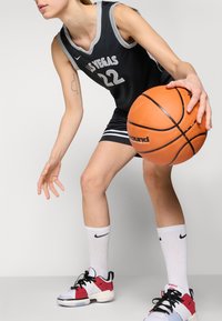 Maillot de basket noir avec "LAS VEGAS" et le numéro "22", associé à des chaussettes blanches montantes et des baskets sportives multicolores, tenant un ballon de basket orange.