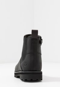 Bota de tornozelo em couro preto com laterais elásticas, aba de puxar texturizada no calcanhar e sola de borracha resistente. Apresenta um logotipo no painel traseiro.