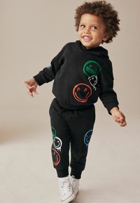 Sorte bomulds hoodie og sweatpants sæt med farverige smiley face grafik i grøn, orange, blå og hvid. Blød tekstur.