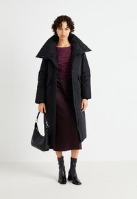 Dug međusobno crni kaput sa visokim ovratnikom, preko bordo i tamnoplave prugaste bluze i saten suknje bordo boje. Crne ankle čizme sa petom.