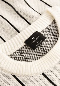 Sweter dzianinowy w białym kolorze z czarnymi pionowymi paskami, z prążkowanym kołnierzem i metką pielęgnacyjną wszytą w dekolt.