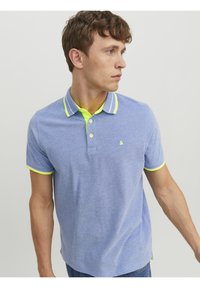 Koszulka polo w jasnoniebieskim kolorze z kontrastującym neonowożółtym kołnierzykiem i wykończeniami rękawów, zapinana na dwa guziki, z małym logo na piersi.
