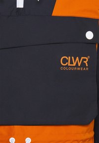 Windbreaker with a black top and orange lower section. Features a front pocket with a snap button and "CLWR COLOURWEAR" logo in orange.