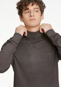 Mörkgrå turtleneck-tröja med ribbad krage och manschetter, tillverkad av ett mjukt, strukturerat material, med en liten broderad logotyp på bröstet.