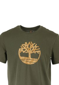 T-shirt in cotone verde oliva con una grafica color sabbia di un albero e un design circolare. Collo a giro classico e maniche corte. Texture morbida.