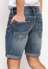 Denim shorts with a faded blue color, rolled cuffs, and a five-pocket design. Features visible stitching and a tag on the waistband.