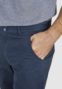 Marineblaue Baumwollchinos mit glatter Textur, ausgestattet mit Seitentaschen und einem Knopfverschluss mit dekorativem Akzent.