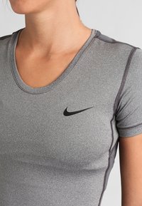 T-shirt de sport gris ajusté à manches courtes, coutures flatlock et logo Nike noir sur la partie supérieure gauche. Texture lisse.