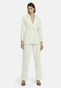 Weißes doppelt geführtes Blazer mit Revers, seitlichen Taschen und passenden weiten Hosen, kombiniert mit schwarzen offenen Absatzschuhen.
