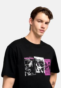 Camiseta negra de manga corta con un estampado gráfico de carteles de conciertos en rosa y blanco, mostrando nombres de bandas y detalles del evento.