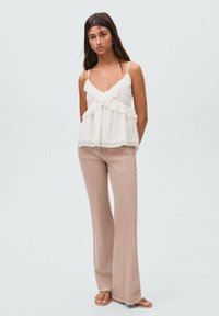 Witte, mouwloze, gerimpelde blouse met een vloeiende uitstraling, gecombineerd met lichtbeige, flare broeken en platte sandalen. Gladde textuur, casual uitstraling.