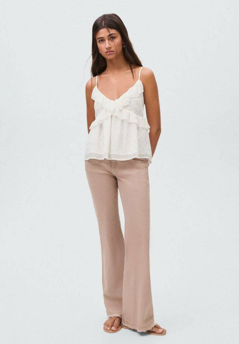 Witte, mouwloze, gerimpelde blouse met een vloeiende uitstraling, gecombineerd met lichtbeige, flare broeken en platte sandalen. Gladde textuur, casual uitstraling.