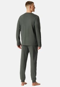 Conjunto de ropa de estar por casa ajustado en verde oscuro. Parte superior de manga larga con cuello redondo y pantalones ajustados a juego. Textura suave, diseño minimalista.