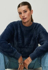 Maglione fuzzy blu navy con maniche lunghe e collo rotondo, abbinato a jeans in denim azzurri e bracciali d'argento a strati.