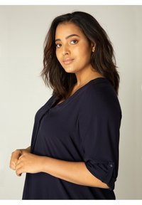 Navy blauwe top met driekwart mouwen van zachte stof, met een gedrapeerde voorkant en opgerolde mouwen. Dit shirt heeft een relaxte pasvorm en een minimalistisch ontwerp.