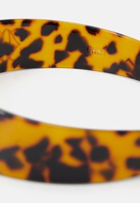 Bandeau à motif écaille de tortue en plastique brillant, présentant des nuances d'orange et de noir avec une finition lisse et un design légèrement courbé.