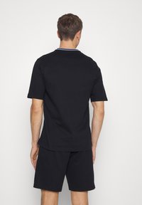 Sort kortærmet polo-shirt med et enkelt design og en krave med en kontrasterende kant. Båret med matchende sorte shorts, vist fra ryggen.