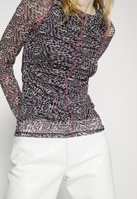 Top a maniche lunghe in tessuto trasparente con un motivo geometrico in nero, bianco e rosa, dettagli in cucitura rosa e texture arricciata.