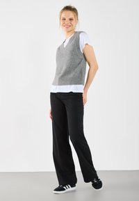 Grå stickad väst över en vit t-shirt, matchad med svarta vida byxor och svarta sneakers. Släta ytstrukturer och enkel design.