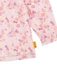Blusa floreale rosa chiaro con piccoli fiori multicolore. Polsini e orlo elasticizzati, con un'etichetta gialla con il logo di un orso.