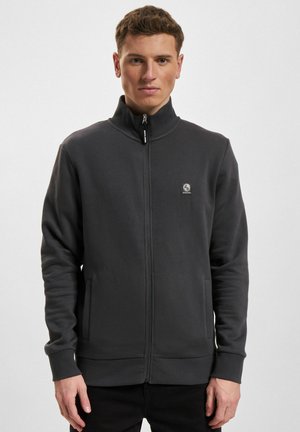 Grå hettegenser med glidelås, laget av mykt stoff. Har høy krage, sidelommer og en liten logo på brystet. Glatt tekstur.