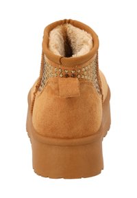 Stivale alla caviglia in suede beige con superficie testurizzata, accenti elasticizzati e una morbida fodera in pelliccia sintetica. Caratterizzato da una suola piatta in gomma e un tassello decorativo sul tallone.