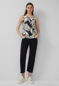Mouwloze zwart-wit bloemen tanktop, zwarte cropped broek en witte sneakers. De top heeft een bladerenpatroon en een ronde halslijn.