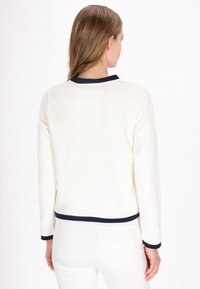 Cream-colored sweatshirt with long sleeves, navy ribbed collar and hem, smooth fabric texture, and a fitted silhouette.