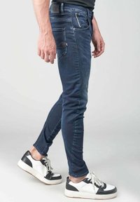 Jeans skinny azul oscuro con un bolsillo frontal, bolsillos traseros y un ligero desgastado. Combinados con zapatillas de deporte en blanco y negro.
