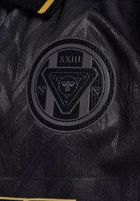 Svart tyg med en cirkulär pr präglad logotyp med en central design och texten "XXIII." Texturerad bakgrund med subtila mönster.