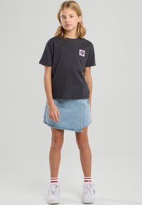 Mustat puuvillapaidat, joissa on vaaleanpunainen auringonlogo vasemmassa rinnassa, yhdistettynä vaaleansiniseen farkuhameeseen. Valkoiset tennarit, joissa on punaiset raidat.