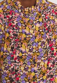Bluse med blomstermønster og farverige små blomster, flæsekrave, knaplukning fortil og flæsedetaljer langs brystet og skuldrene.