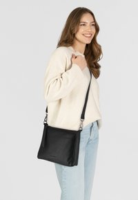 Borsa a tracolla nera in pelle con cintura regolabile, texture liscia, forma rettangolare, dotata di accenti metallici e branding minimalista.