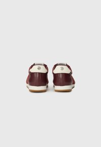Un paio di sneakers basse bordeaux e bianche viste da dietro su uno sfondo bianco.