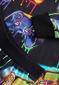 Material negru cu un grafic colorat al unui controler de jocuri video cu picături de vopsea, însoțit de manșete și talie cu dungi negre.