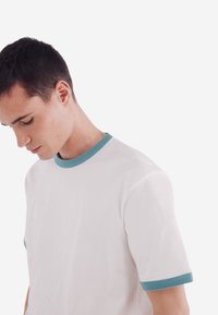 Weißes Baumwoll-T-Shirt mit kurzen Ärmeln, ausgestattet mit hellblauer gerippter Kragen- und Ärmelakzenten, glatter Textur und lockerem Schnitt.