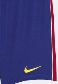 Pantaloni Nike in un vivace tessuto blu, con una striscia laterale rossa con dettagli gialli e un piccolo logo Nike giallo sull'orlo.