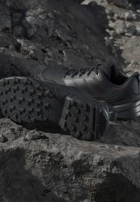 Black hiking shoes with rugged tread soles resting on dark rocky terrain, highlighting durability and outdoor use.