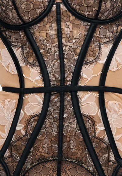 Corset en dentelle noire et beige avec motifs floraux et baleinage structuré sur tissu transparent.