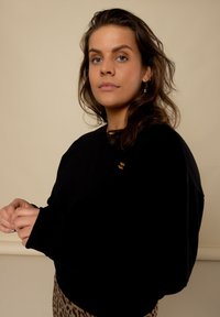 Zwarte sweatshirt met een ontspannen pasvorm, geribde mouwen en een klein gouden logo op de borst; gedragen met een panterprint rok.