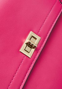 Hett rosa läder med en slät yta, med ett rektangulärt lås i guldton fram och kontrasterande svart sömnad längs kanterna.