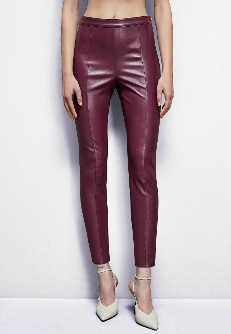 Leggings in pelle bordeaux con vestibilità slim, dotati di vita alta e texture liscia, abbinati a scarpe con tacco di colore crema.