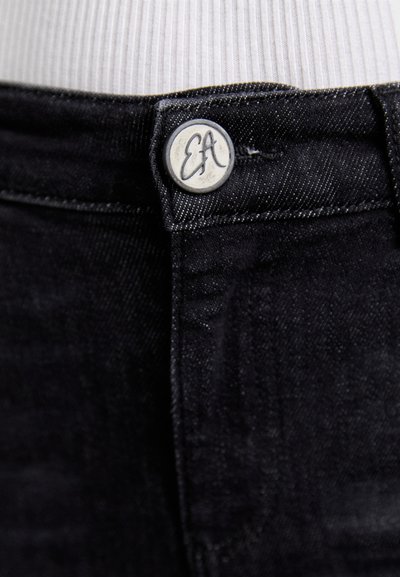 Mustat denim-farkut sisältävät metallinappulan, jossa on kaiverrettu "EA", sileän pinnan, kapean muotoilun ja hillityn kontrastivärisen ompelun vyötärön kohdalla.